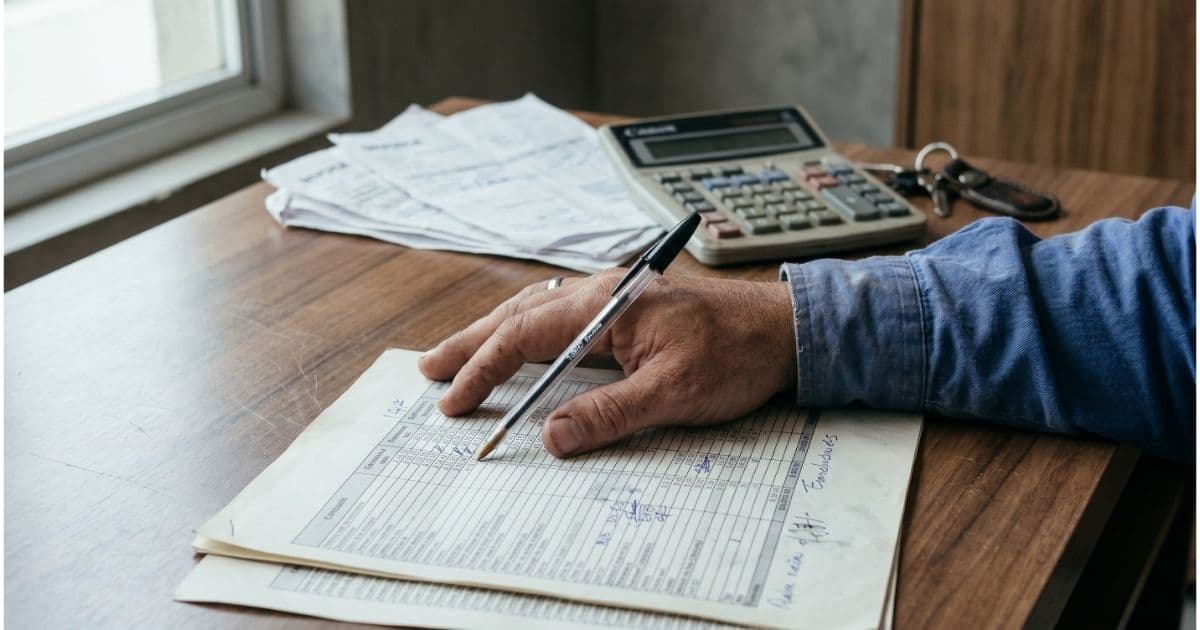 Mão sobre planilha de controle manual de frota com calculadora e chaves de veículo sobre mesa de madeira